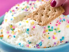 a hand dipping a cracker into a bowl of ice cream with sprinkles