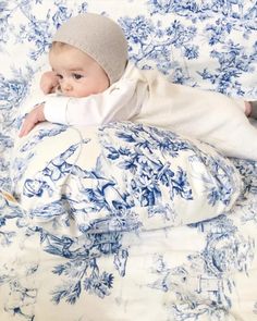 a baby laying on top of a bed covered in blue and white sheets with a knitted hat