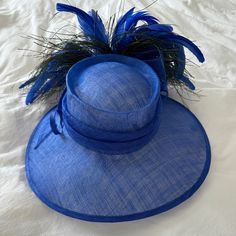 Mad Hatter Kentucky Derby Hat With Feathers And Wide Brim. Blue. String Tightens Head Piece. Kentucky Derby Racetrack Hat. Peacock Like Feathers Blue Fedora Sun Hat For Kentucky Derby, Blue Fedora Straw Hat For Kentucky Derby, Adjustable Blue Fedora Straw Hat, Blue Adjustable Cloche Hat For Summer, Elegant Blue Fedora With Short Brim, Blue Mini Hats With Curved Brim For Beach, Blue Mini Hat With Curved Brim For Beach, Blue Curved Brim Mini Hat For Beach, Adjustable Blue Costume Hats With Curved Brim