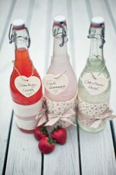 three bottles filled with liquid sitting on top of a wooden table next to a strawberry