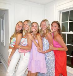 four beautiful young women standing next to each other in front of a white wall and window