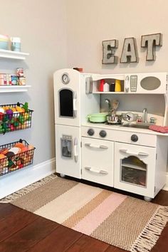 a play kitchen with white cabinets and wooden floors