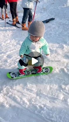 a young child riding a snowboard down a snow covered slope with other skiers in the background