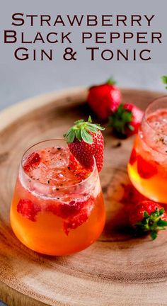 two glasses of strawberry black pepper gin and tonic sitting on a wooden tray with strawberries