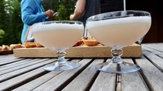 two glasses filled with white liquid sitting on top of a wooden table