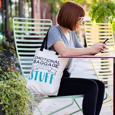 a woman sitting at a table with a tote bag and cell phone in her hand