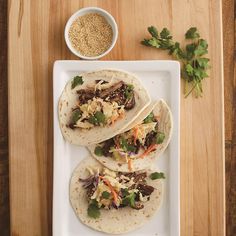 three tacos on a white plate next to a bowl of rice and cilantro