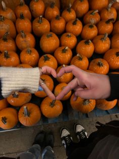 two people making a heart with their hands in front of a pile of pumpkins