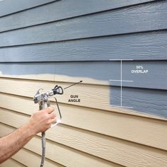 a man spray painting the side of a house with blue siding and white paint on it