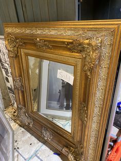 a gold framed mirror sitting on top of a floor next to a pile of tools