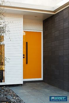 an orange front door sits next to a black and white house with rocks on the ground