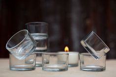 three clear glass cups sitting on top of a table next to a lit candlestick