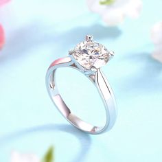 a white diamond ring sitting on top of a blue surface next to flowers and petals