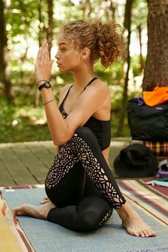 a woman sitting on top of a yoga mat in the middle of a wooded area