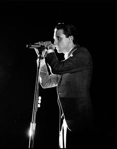 a black and white photo of a man singing into a microphone with his hands in the air