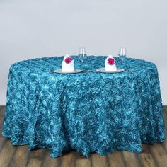 two glasses are sitting on top of a table covered with a blue cloth and red rose petals