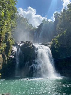 a large waterfall in the middle of a forest filled with green trees and blue water