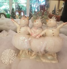 three snowmen dressed in white tulle and tiaras on top of a table