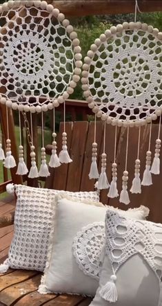 some white pillows are sitting on a wooden bench with tassels hanging from it