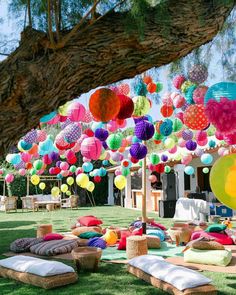 many colorful balloons and pillows are hanging from the trees in front of an outdoor party