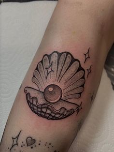 a black and white photo of a shell tattoo on the left arm with stars around it