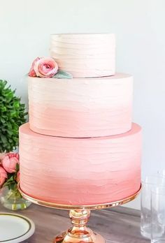 a three tiered cake with pink icing and flowers on top, sitting on a table