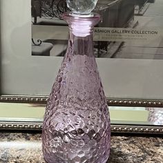 a pink glass bottle sitting on top of a counter next to a framed photo in a frame