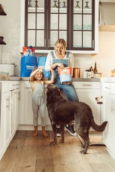 a woman and her daughter are in the kitchen with their dog