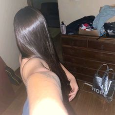 a woman with long hair sitting on the floor in front of a dresser and purse