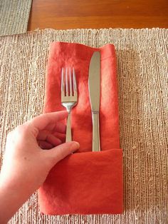 a person holding a fork and knife on top of a red napkin next to an orange napkin