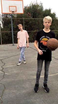 two young boys playing basketball on an outdoor court with one holding a ball in his hand