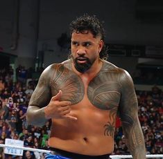 a man with tattoos on his chest standing in front of a crowd at a wrestling match