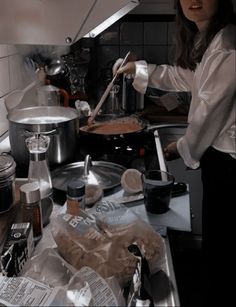 a woman cooking food in a kitchen with pots and pans on the stove top