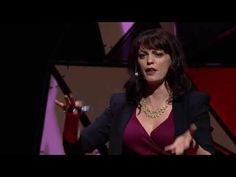 a woman in a purple shirt and black blazer talking on stage with her hands out