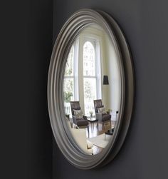 an oval mirror hanging on the wall in front of a living room with two chairs