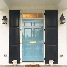 a blue front door with black shutters and potted plants