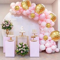 pink and gold balloons are hanging from the ceiling in front of a cake table with flowers