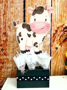 a cow standing on top of a wooden table next to flowers and paper machs