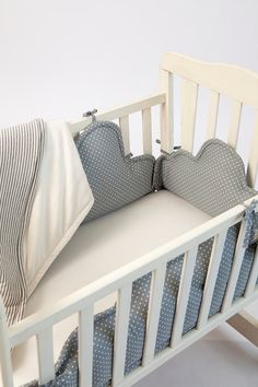 a baby crib with blue and white pillows on it's sides, in front of a white wall