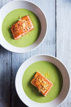 two white bowls filled with green soup on top of a wooden table next to each other