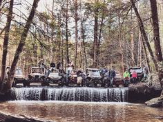 a group of people standing around four wheelers in the woods