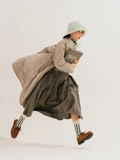 a woman in a dress and hat is holding a book while running with her legs spread out