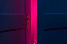 two doors are lit up with pink and blue light in the dark room, one is open