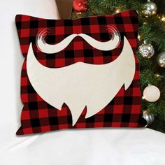 a red and black plaid pillow with a white beard on it next to a christmas tree