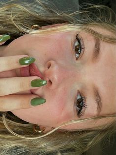 a woman with green nail polish holding her hand up to her face and looking at the camera