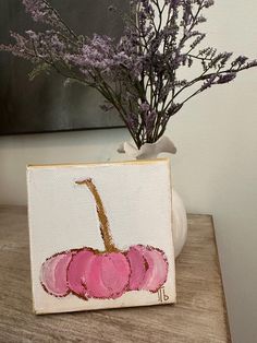 a vase with purple flowers in it sitting on a table next to a small painting