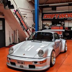 a silver sports car parked in a garage next to some stairs and an orange floor