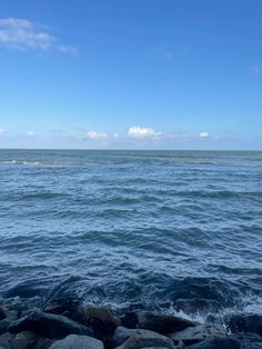 an ocean view with rocks in the foreground and water on the far side under a blue sky