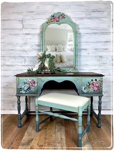 a blue vanity with flowers painted on it and a mirror over the top that has a bench in front of it