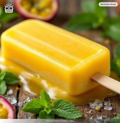 a popsicle is sitting on a wooden table with mint leaves and sliced fruit in the background